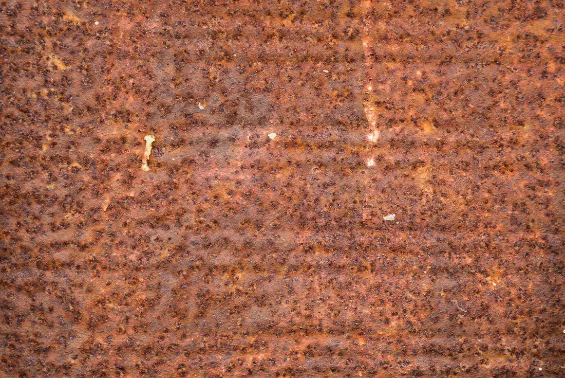 Close-up of a weathered metal surface with peeling blue-green paint and dark orange rust spreading across cracked layers