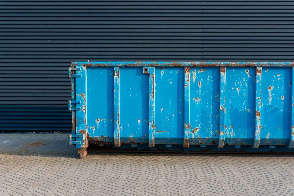 Blue steel skip container standing on block paving against a dark corrugated warehouse wall