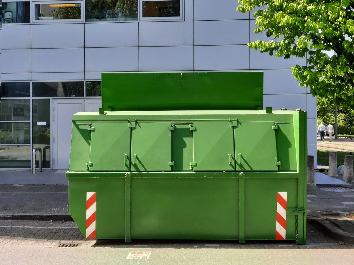Large green lidded waste container parked at the kerb outside a modern office building