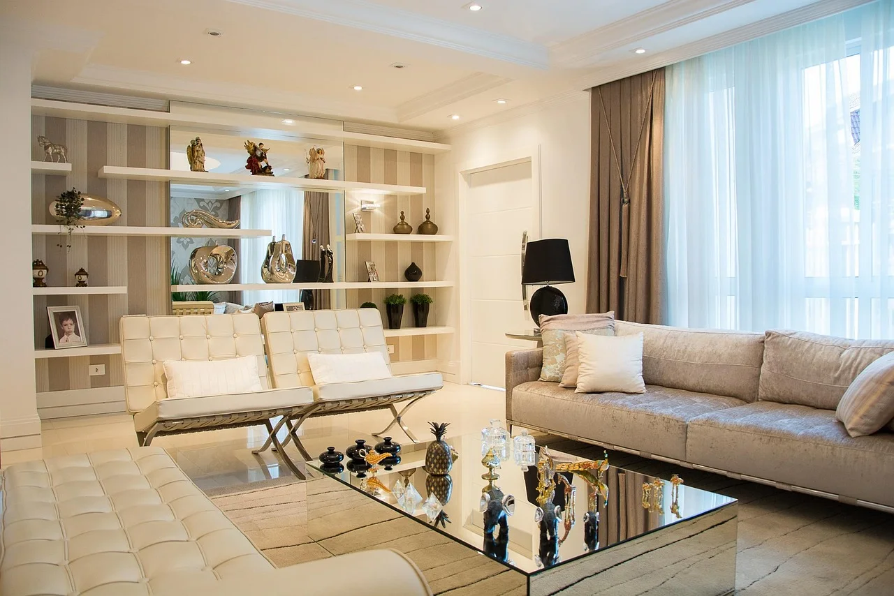 Bright living room with a mirror-topped coffee table reflecting a row of ornaments, cream tufted seating and a mirror-backed display recess along the wall