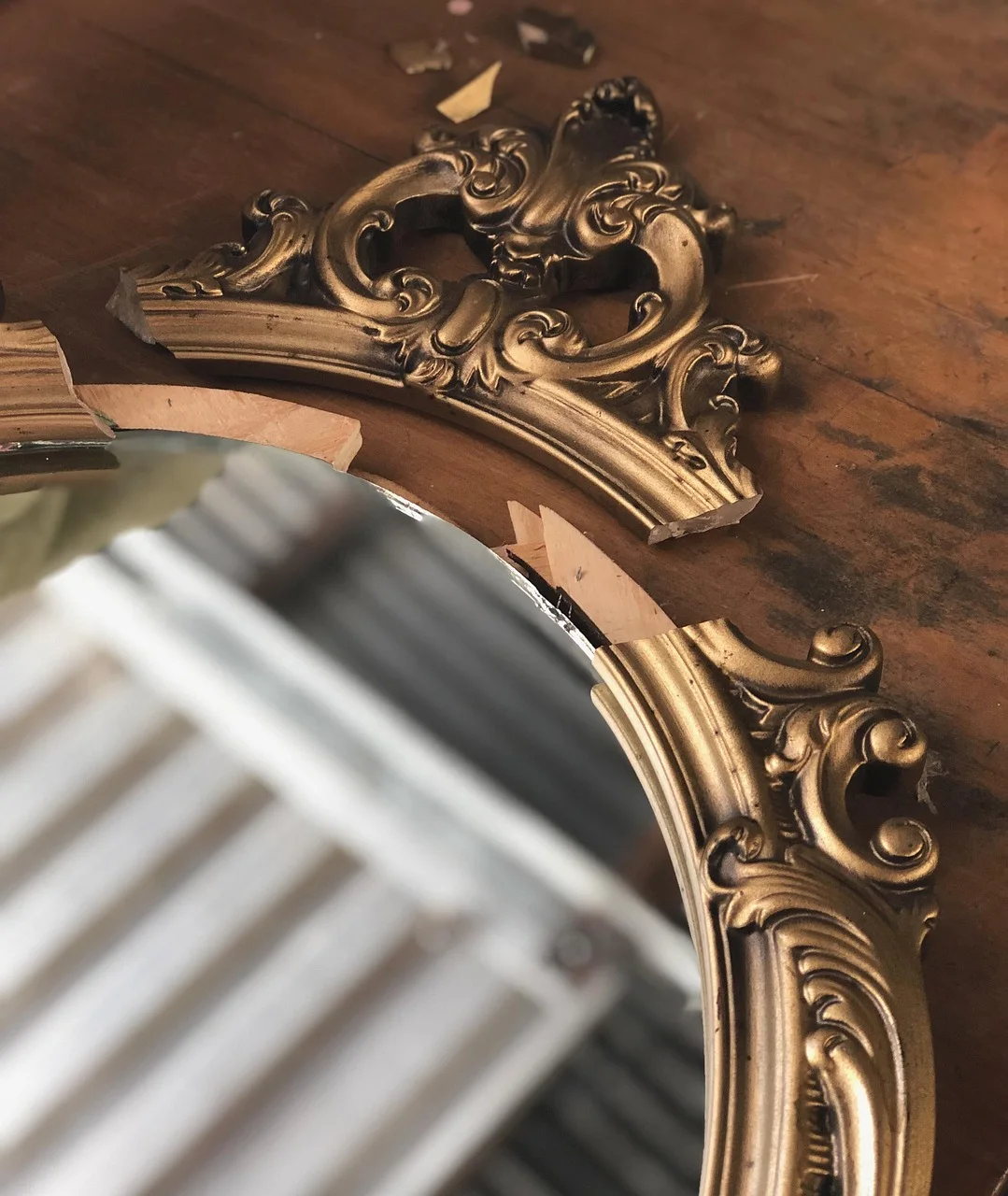Close-up of an ornate carved gilt mirror frame with the bevelled edge of the glass visible, resting face up on a bare wooden floor