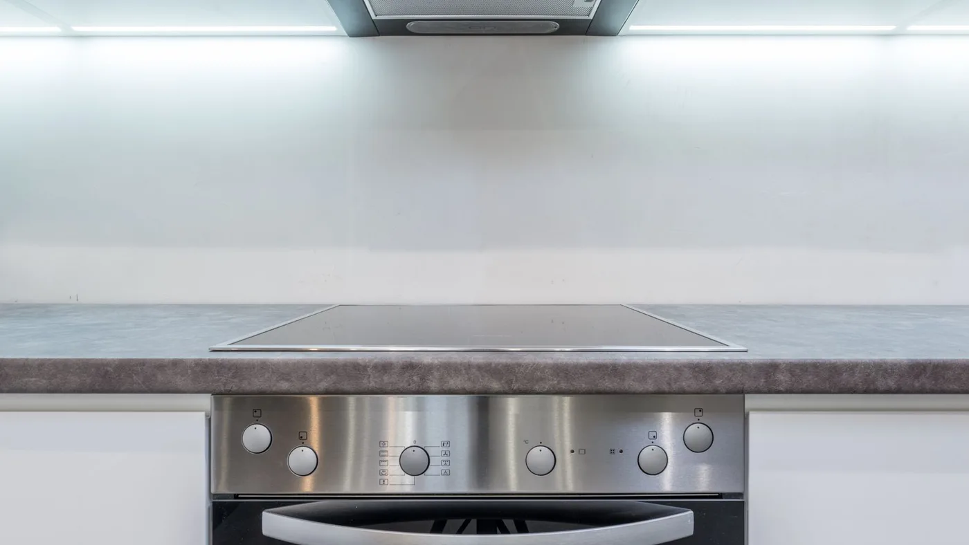 Built-in ceramic hob set into a grey worktop with a stainless integrated oven below and an extractor hood above