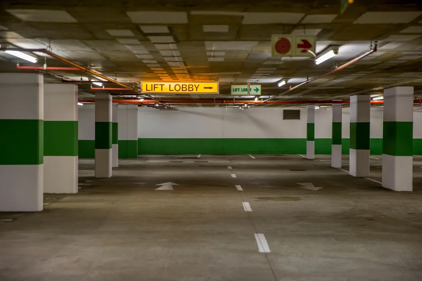 Empty concrete basement car park with marked bays, structural columns and a lift lobby sign
