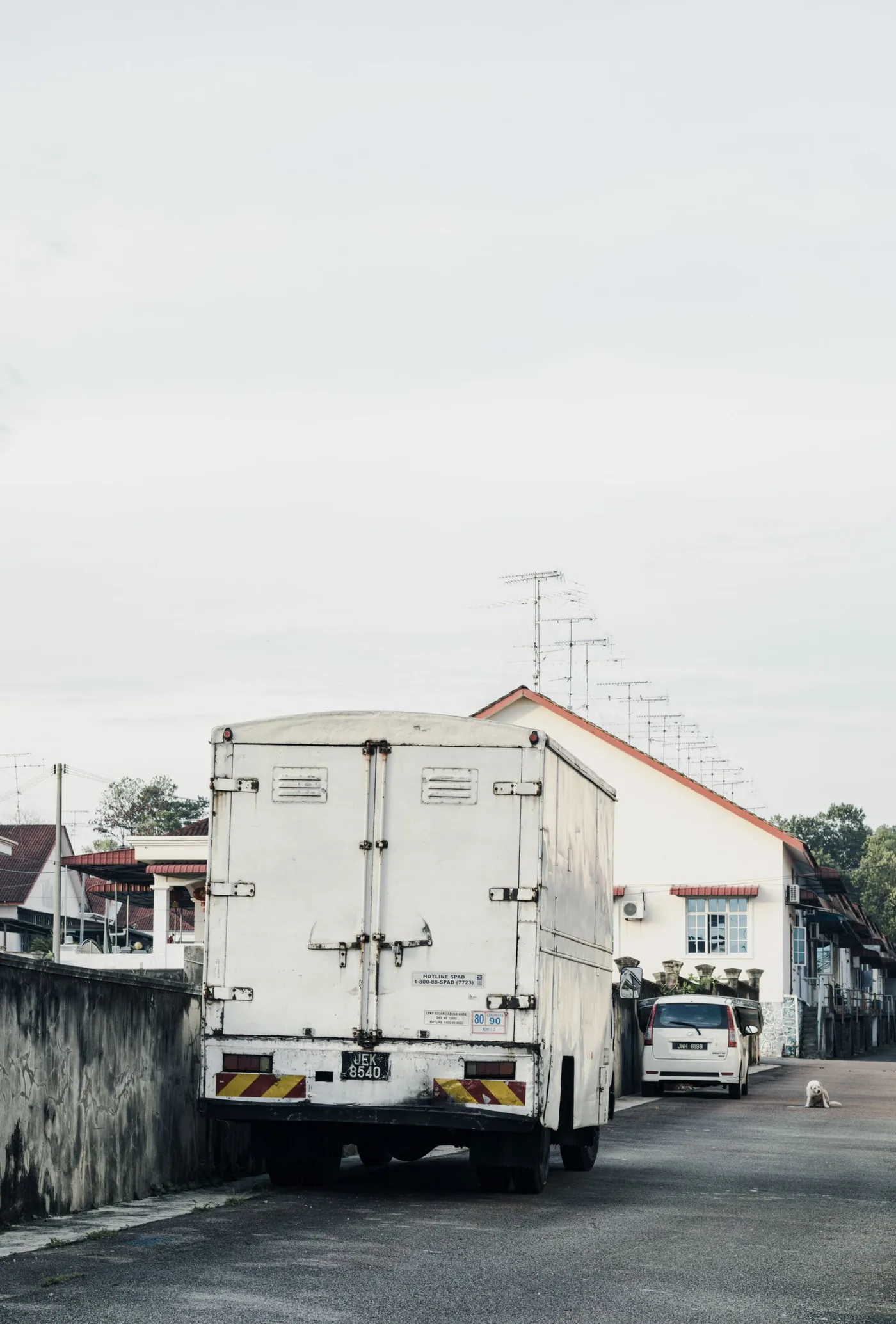 White delivery van parked at the kerb on a quiet residential street with houses behind it