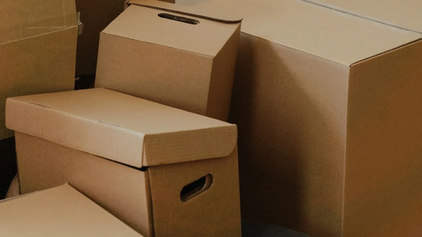 Stack of plain brown cardboard moving boxes and lidded archive cartons piled against a white panelled door