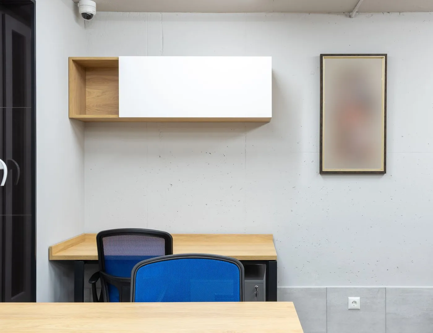 Office corner with a wall-mounted white and oak storage unit above a fitted desk with two blue mesh chairs and a small safe