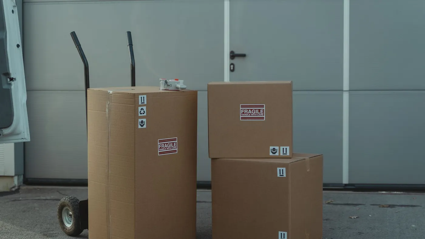 Three cardboard boxes marked fragile stacked beside a hand truck outside a grey loading door