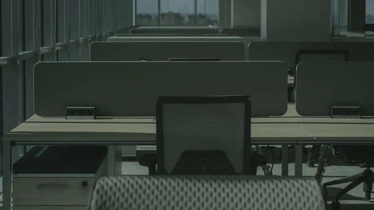 Row of bolted bench workstation desks with privacy screens and cable management in a Dubai office being cleared