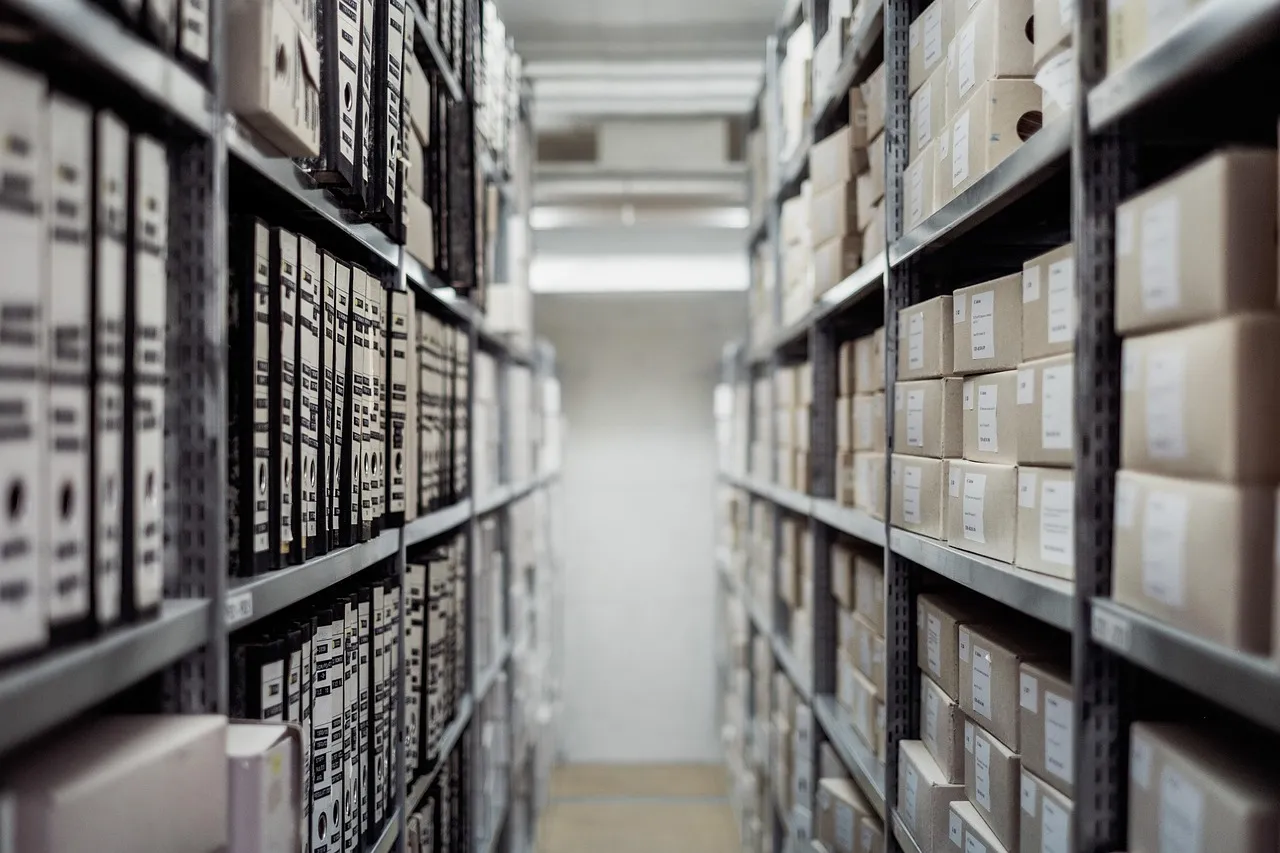 Rows of metal shelving stacked with labelled archive boxes and lever-arch files in a storage corridor