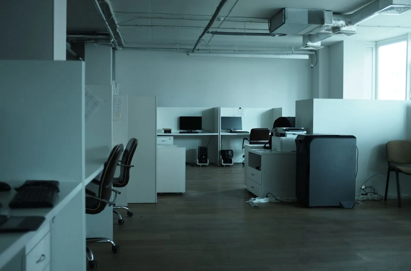 Deserted office with monitors, desktop towers, a large printer and partition screens left behind after a move