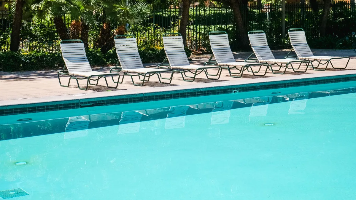 Row of white and green metal sun loungers along the edge of a swimming pool