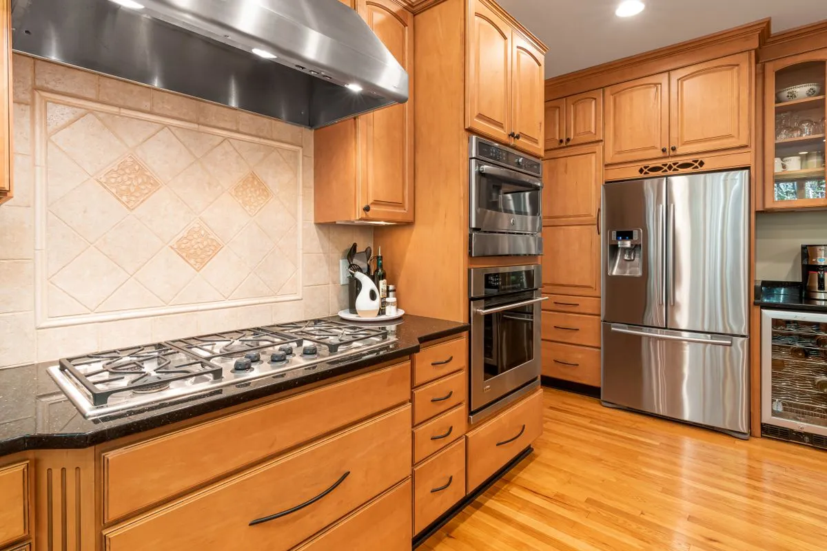 Kitchen with a stainless steel double oven and gas cooktop built into wood cabinetry beneath an extractor hood