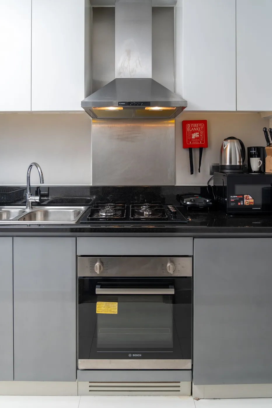 Built-in single oven set beneath a gas hob with an extractor fan above, in a grey and white kitchen