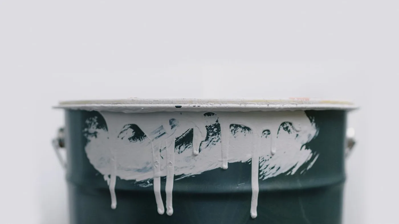 Dark green paint tin with white emulsion dried in thick drips down the outside and across the rim