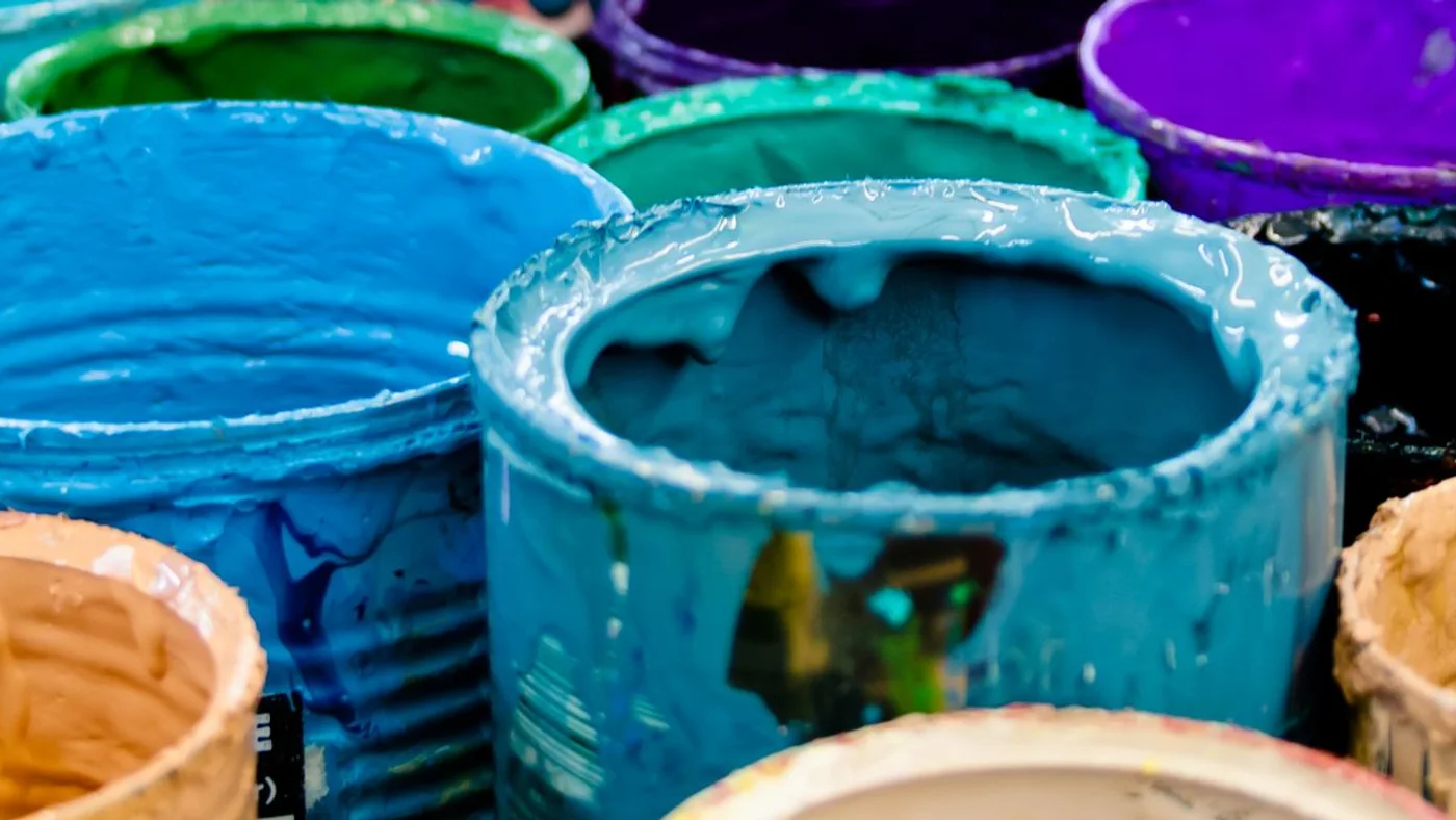 Open tins of blue, teal, green and purple paint packed together, each part used with paint dried around the rims