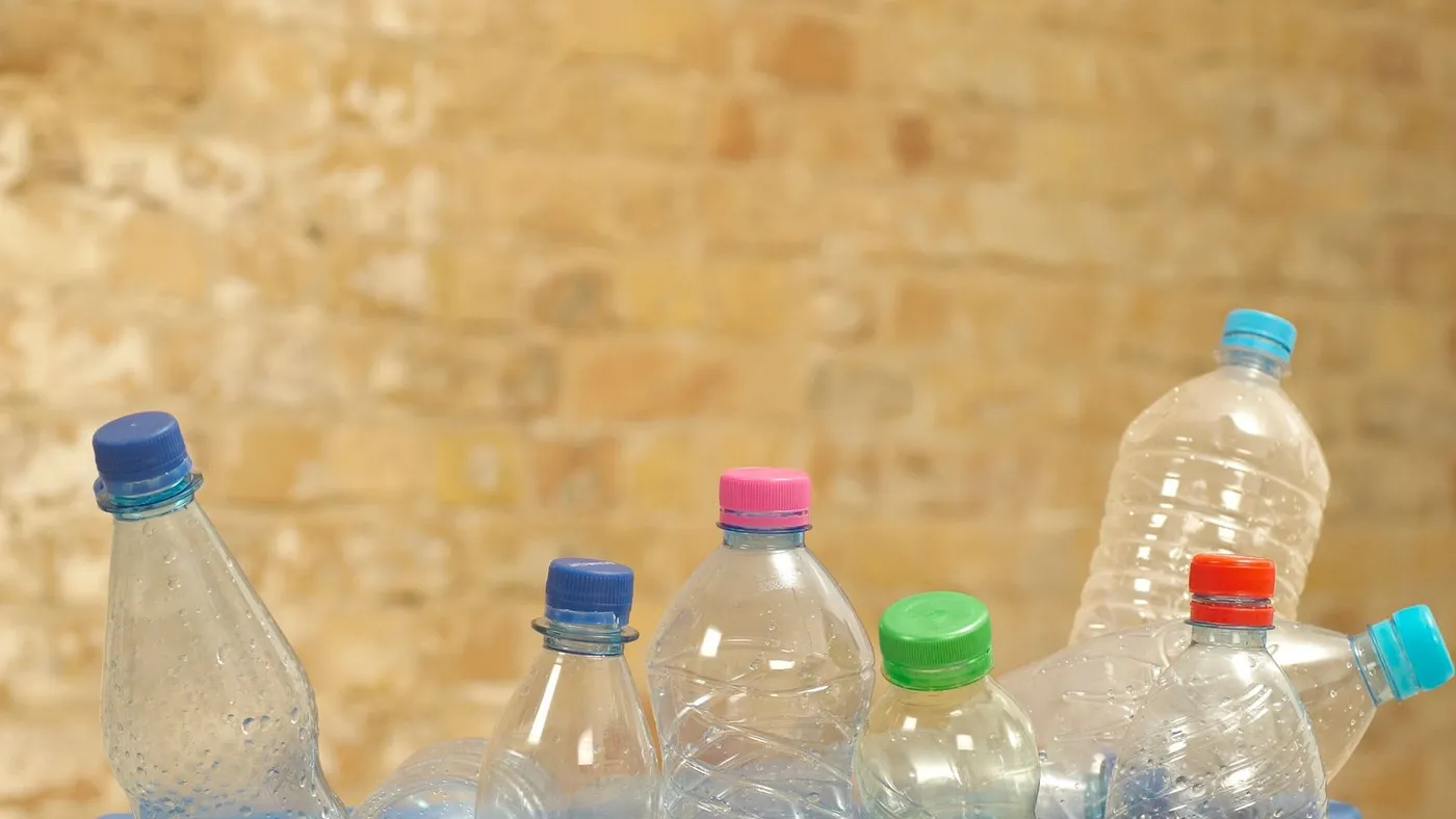 Row of empty plastic bottles with different coloured caps lined up inside a blue crate against a brick wall