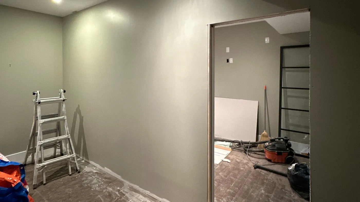 Freshly painted hallway with a stepladder, folded plastic dust sheets and a wet-dry vacuum beside an open doorway during a home renovation