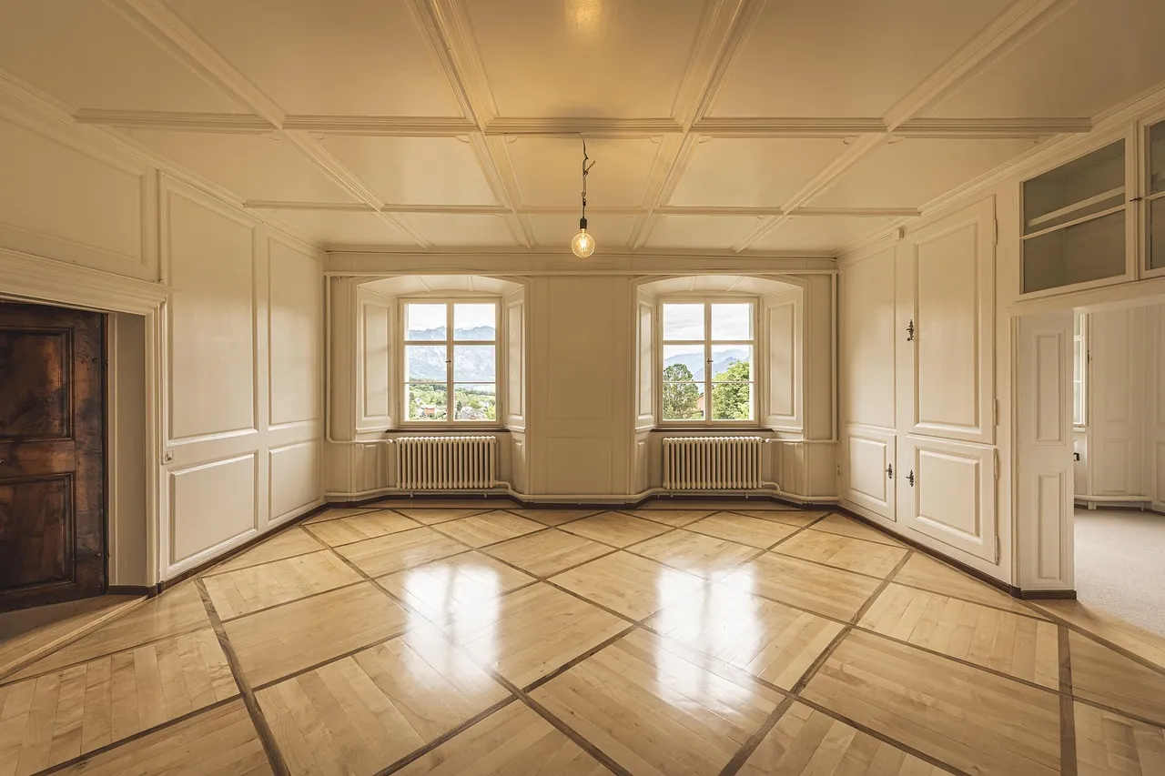 Empty panelled room with a polished parquet floor, two arched windows and no furniture remaining