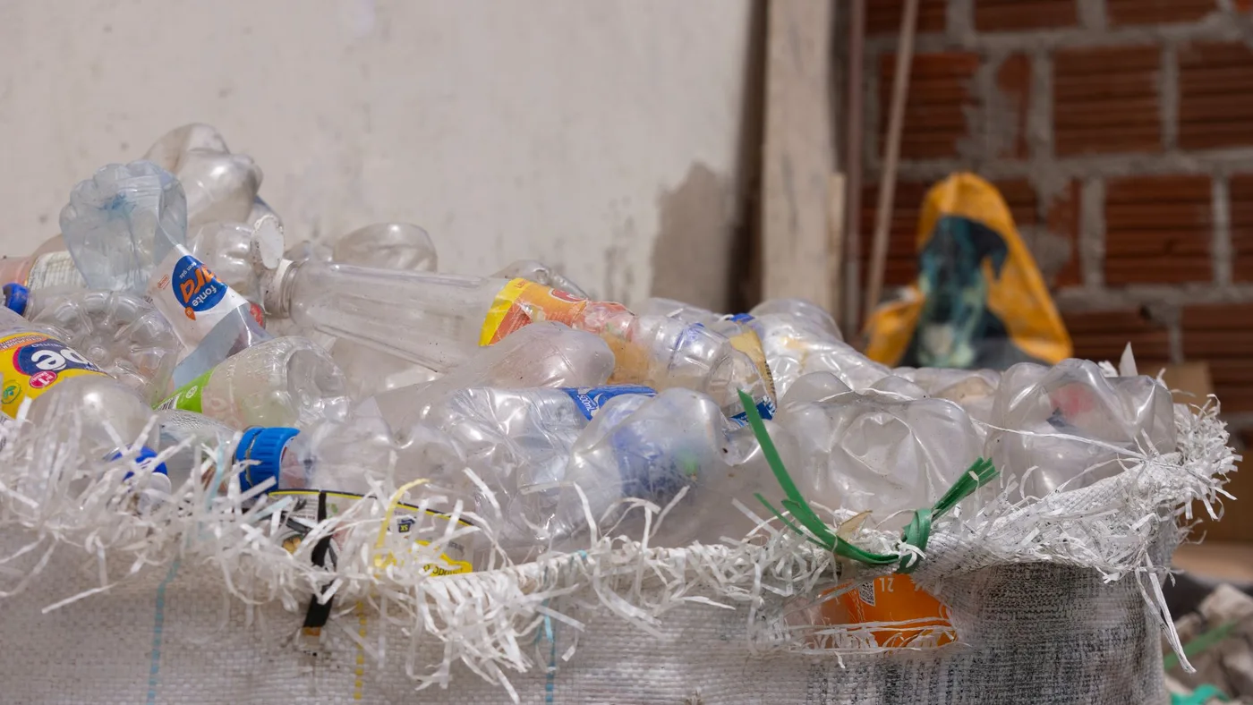 Large mesh collection sack filled with empty clear plastic drinks bottles resting against a brick wall
