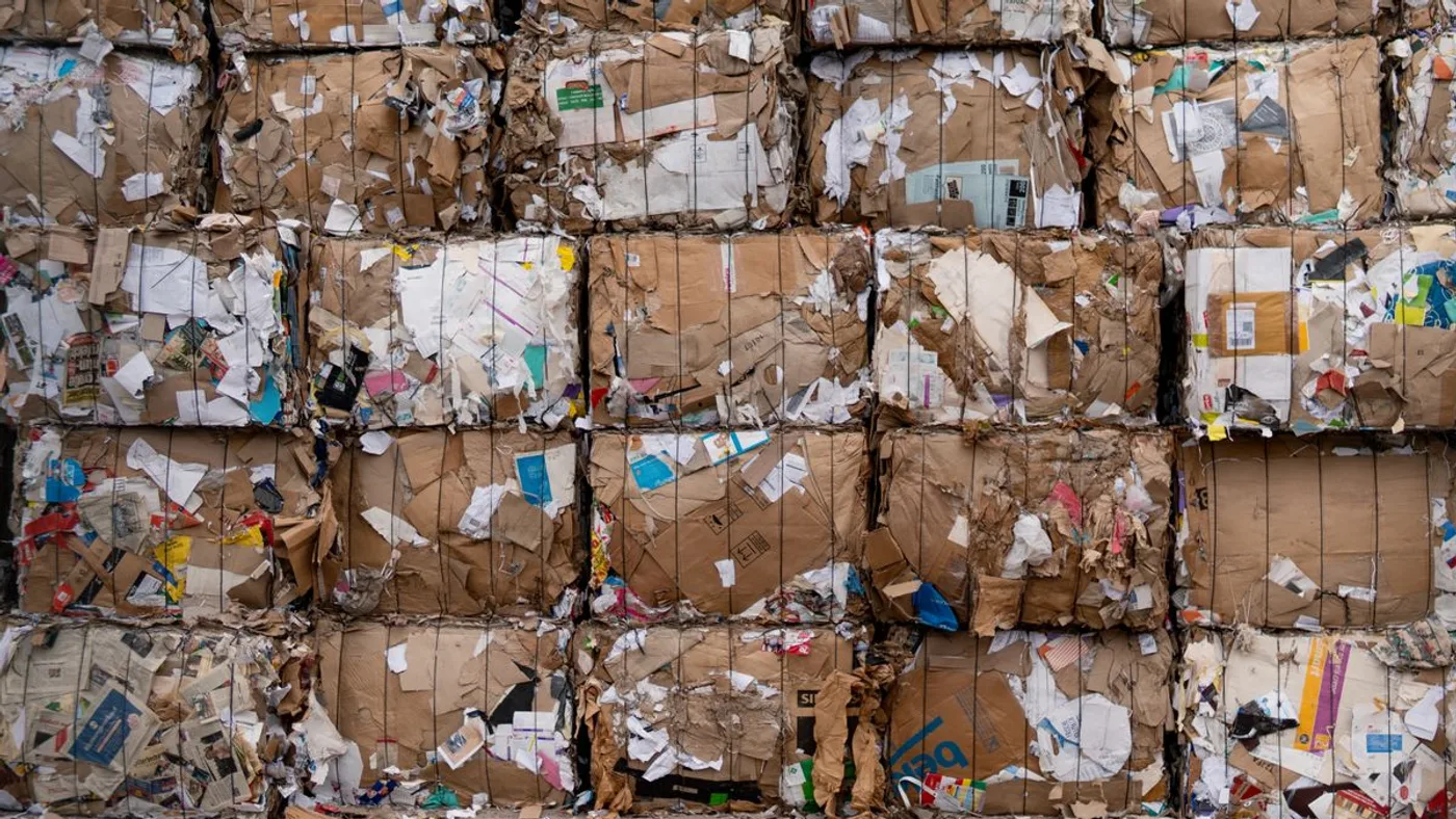 Wall of compressed cardboard and paper bales stacked several rows high and bound with wire