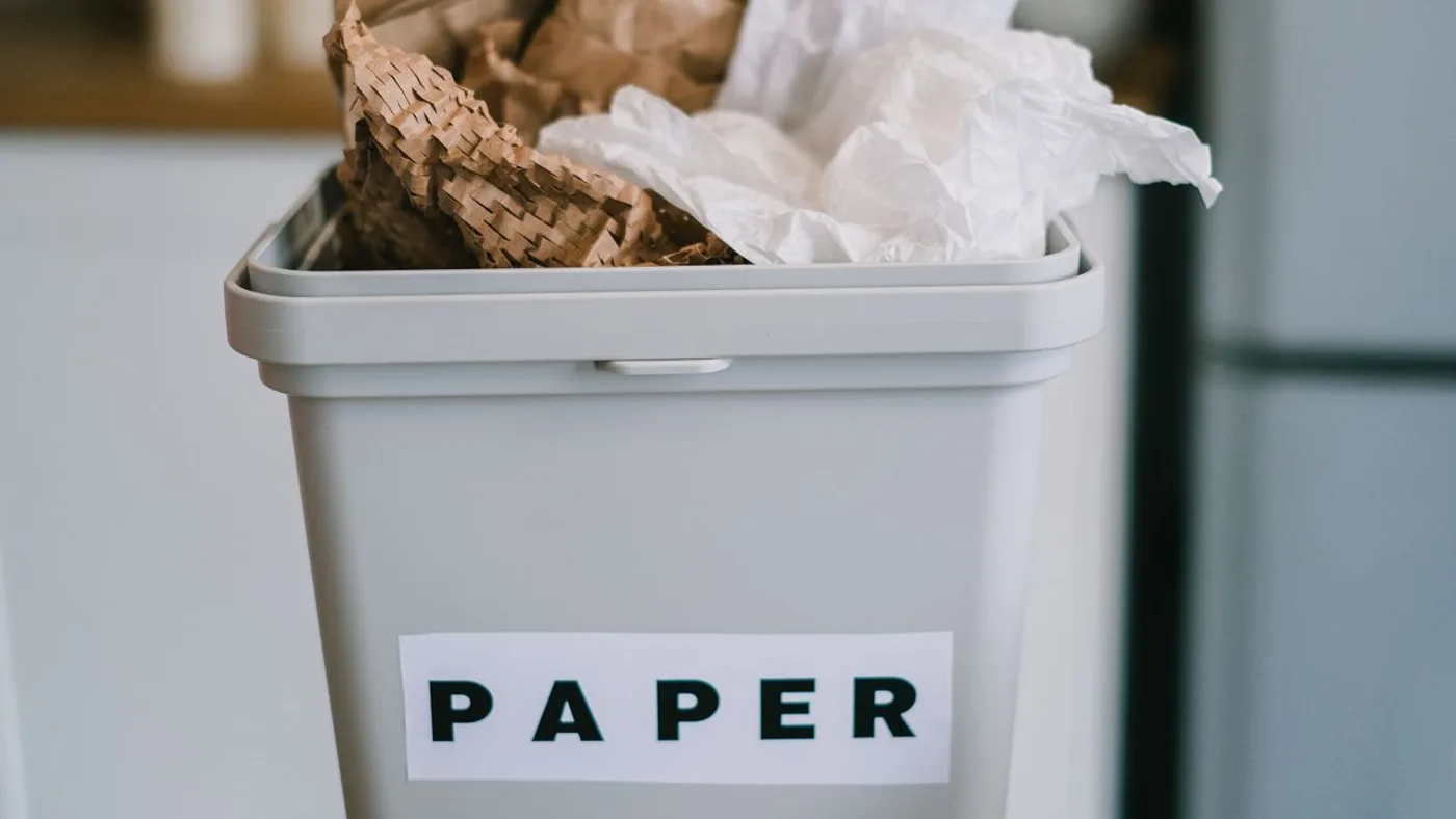Grey kitchen bin labelled PAPER in black capitals, filled with brown packing paper and white tissue