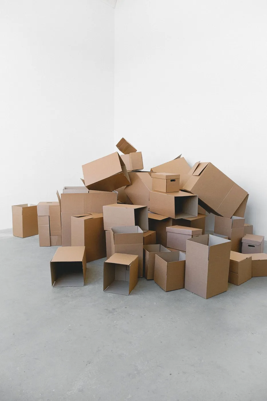 Pile of assorted cardboard boxes stacked in the corner of an otherwise empty white room after a move