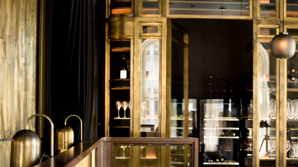 Restaurant bar area with brass and glass back-bar shelving, bottle displays and a polished counter