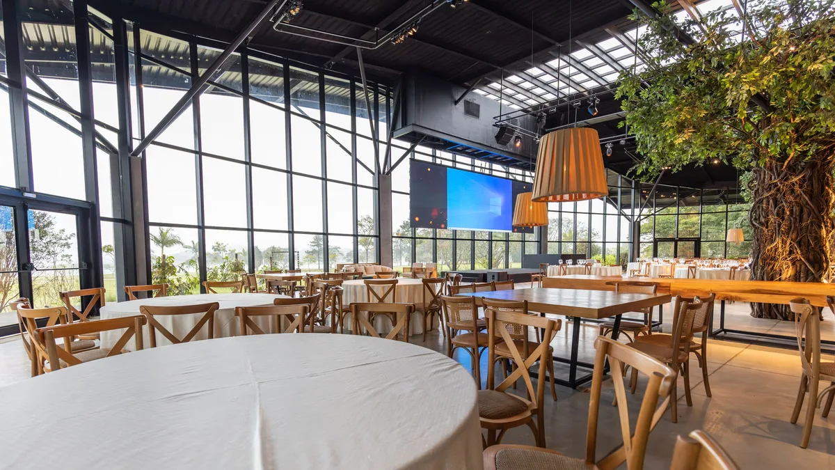 Empty restaurant dining room with wooden chairs and round and rectangular tables beside a full-height glass wall