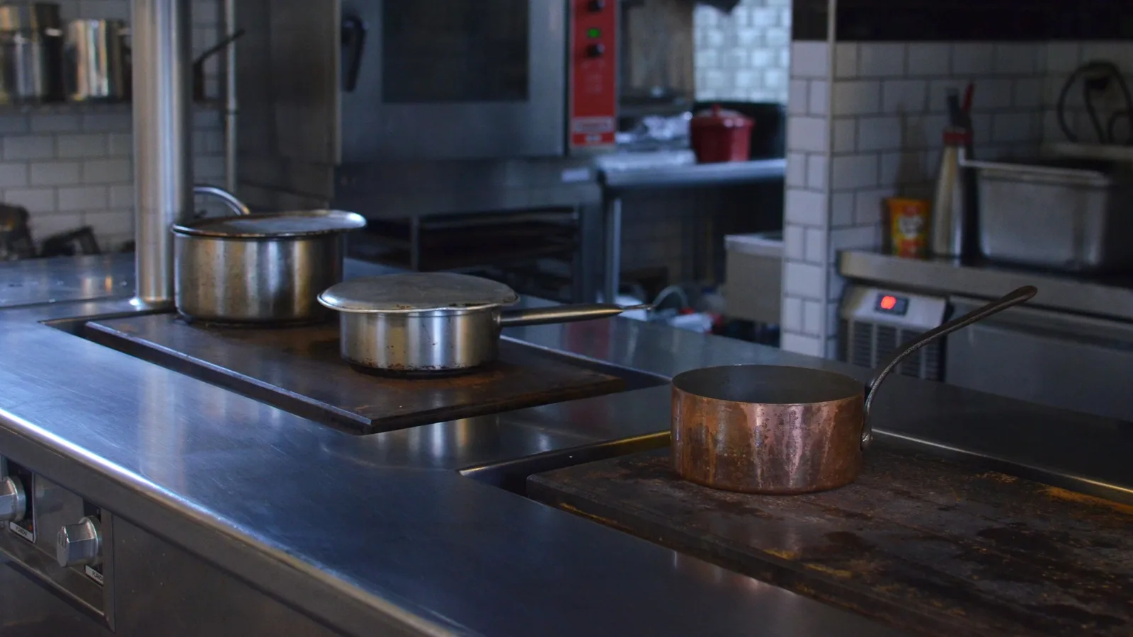 Stainless steel commercial kitchen line in a restaurant with pans on the range and equipment along the back wall