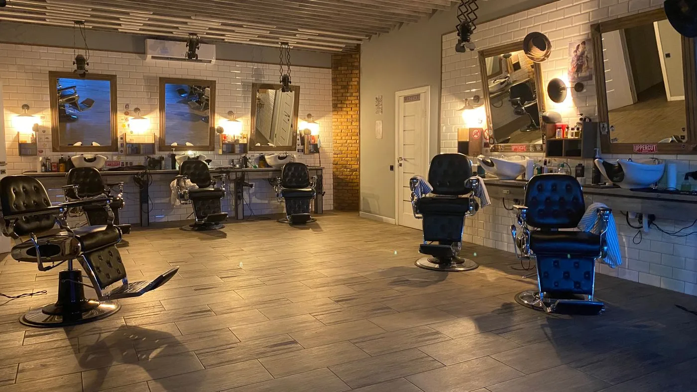 Empty barber shop at night with five chrome and black leather chairs on the tiled floor facing framed mirrors and white wall-mounted wash basins