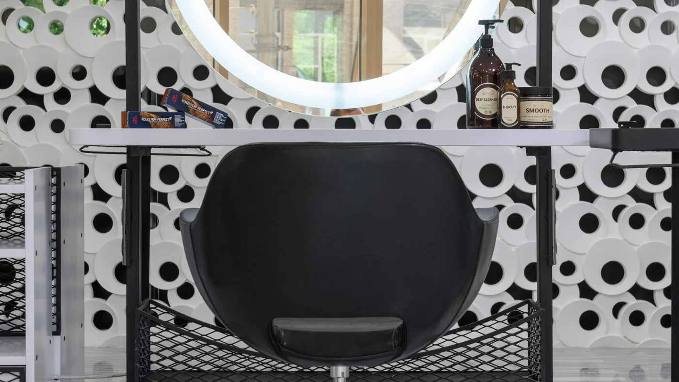 Salon styling station with a black leather chair on a chrome five-star castor base beneath a circular ring-light mirror and shelved product bottles