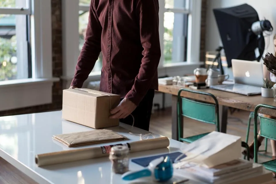 Person taping and preparing a small cardboard box on a table for handoff
