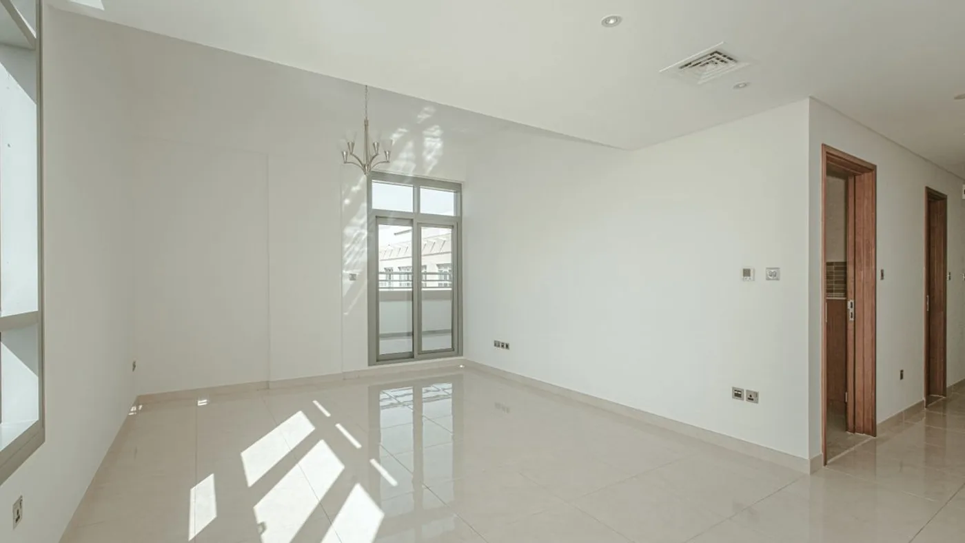 Empty apartment room with polished cream tiled flooring, white walls, ceiling air conditioning vents, a small chandelier and a wooden door
