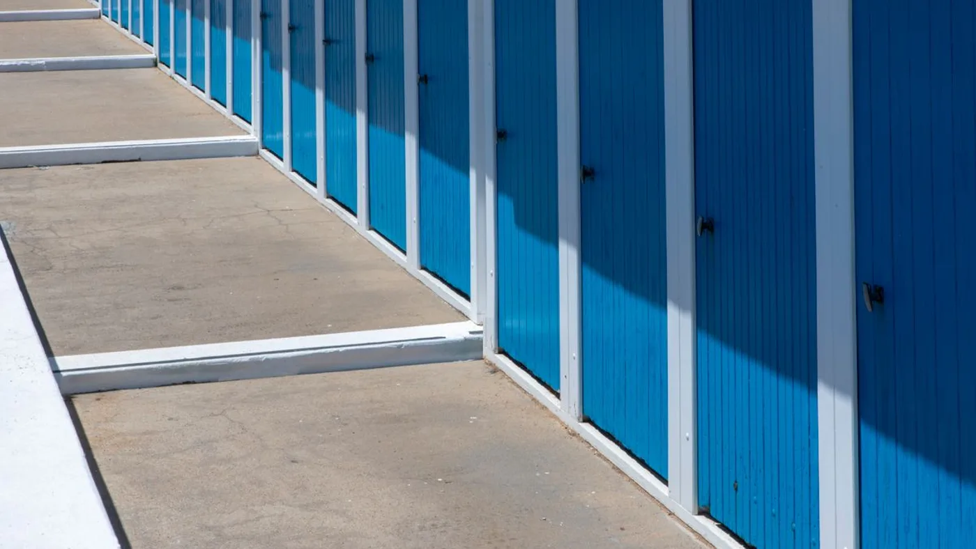 Long corridor inside a self storage facility lined on one side with bright blue roller shutter doors on individual units