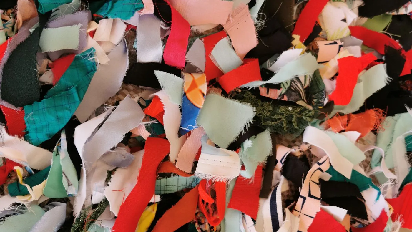 Dense mass of shredded fabric offcuts in red, white, teal and black jumbled together