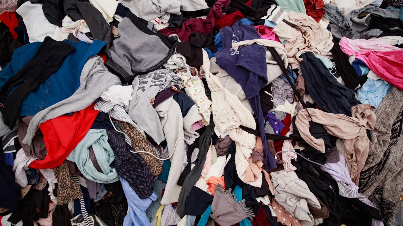 Large heap of mixed discarded clothing in many colours filling the whole frame