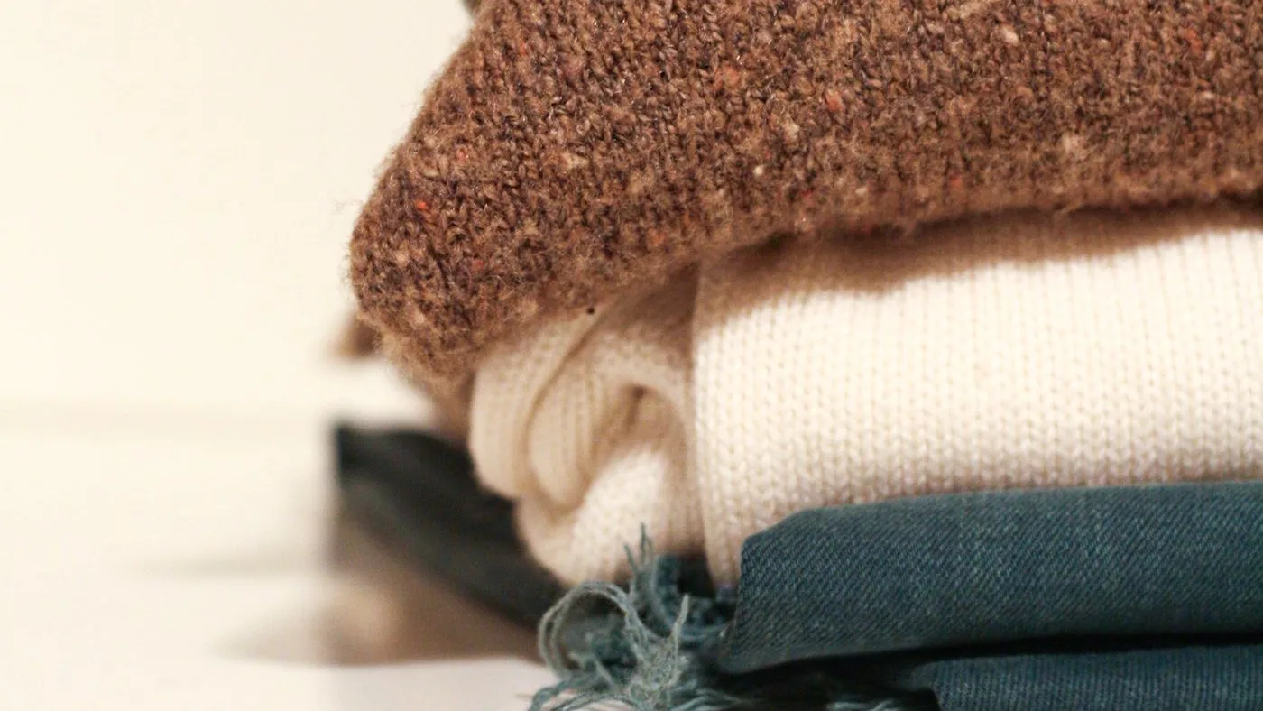 Stack of folded knitwear in brown and cream resting on a teal cotton item with a frayed edge