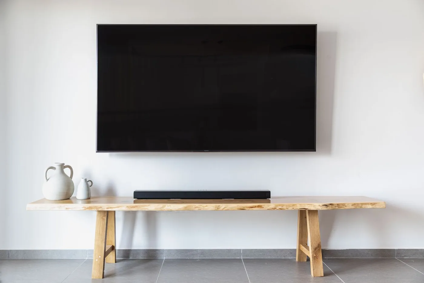 Large wall-mounted flat-screen television above a low live-edge wooden bench holding a soundbar and two vases