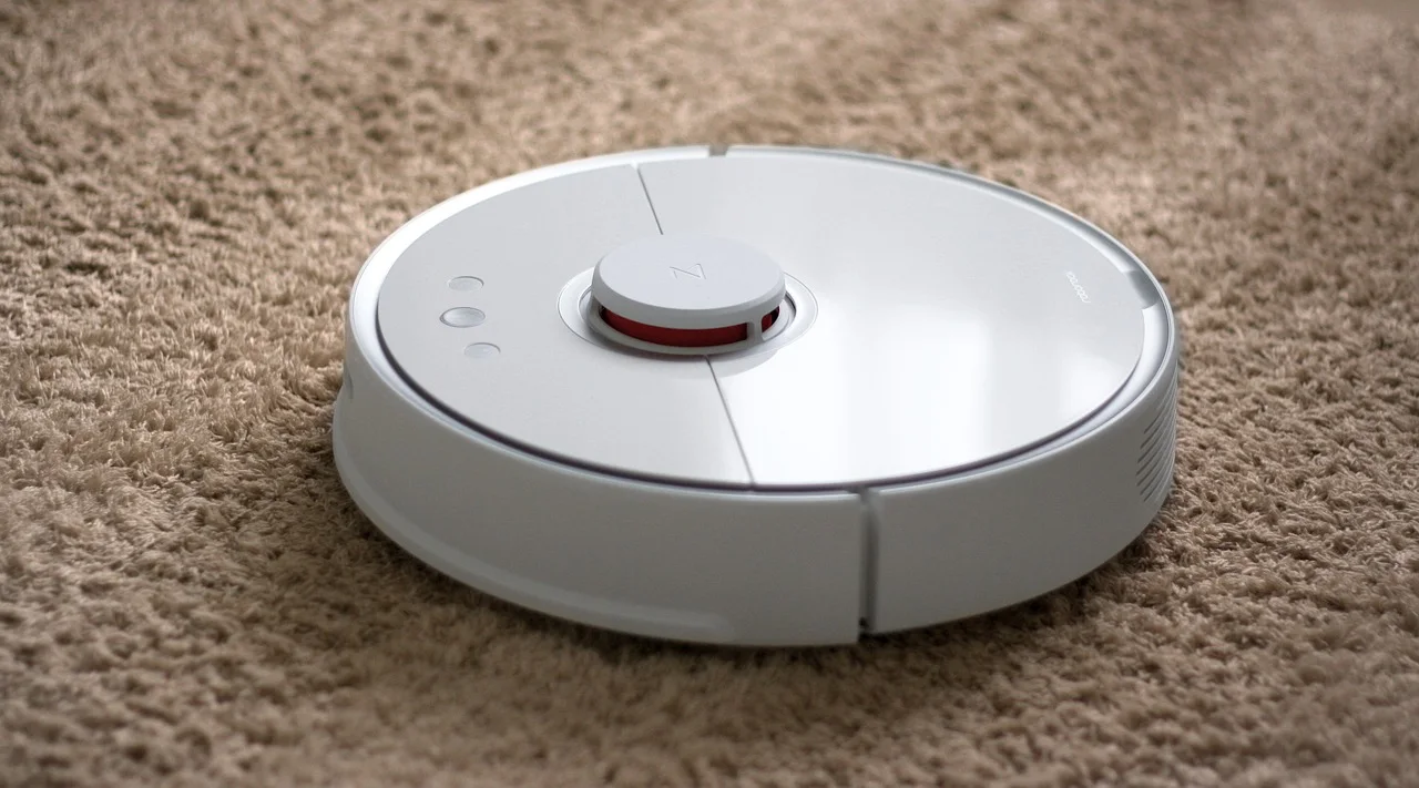 White circular robot vacuum cleaner with a raised laser sensor turret and a recessed control button, sitting on a thick beige carpet