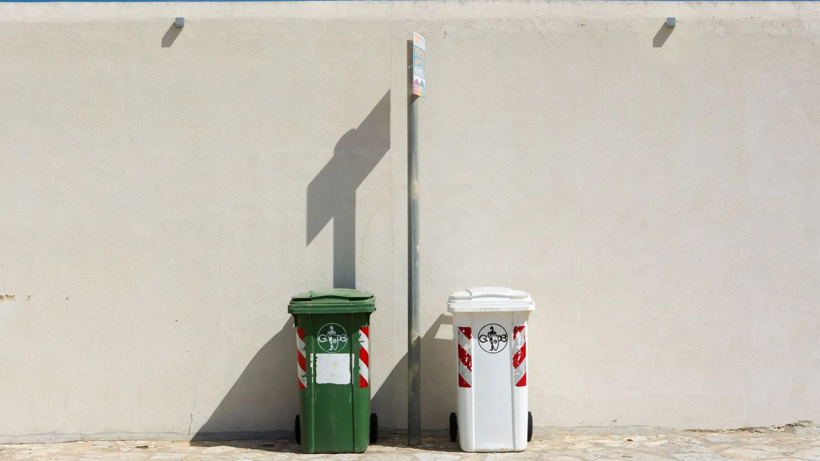 Green and white waste collection bins beside a sunlit wall in Dubai, ready for reliable residential and commercial waste pickup