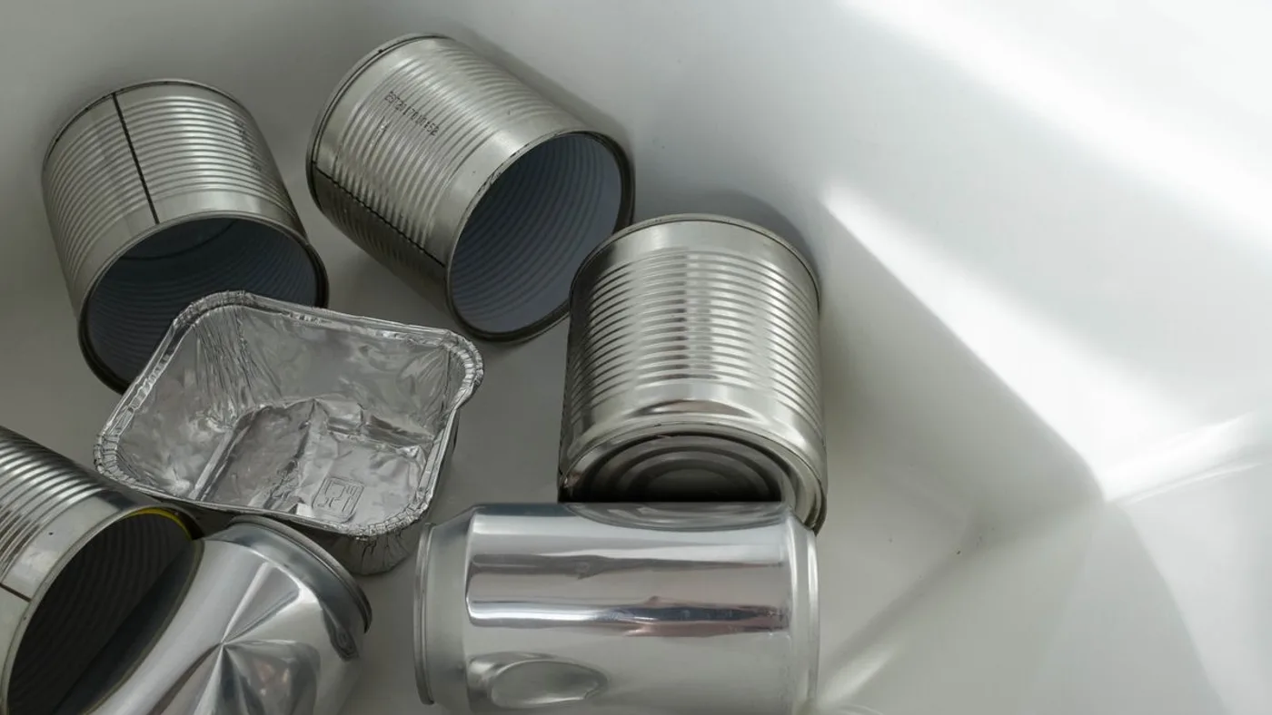 Rinsed metal food tins, aluminium drink cans and a foil tray with their labels removed, sitting in a white container