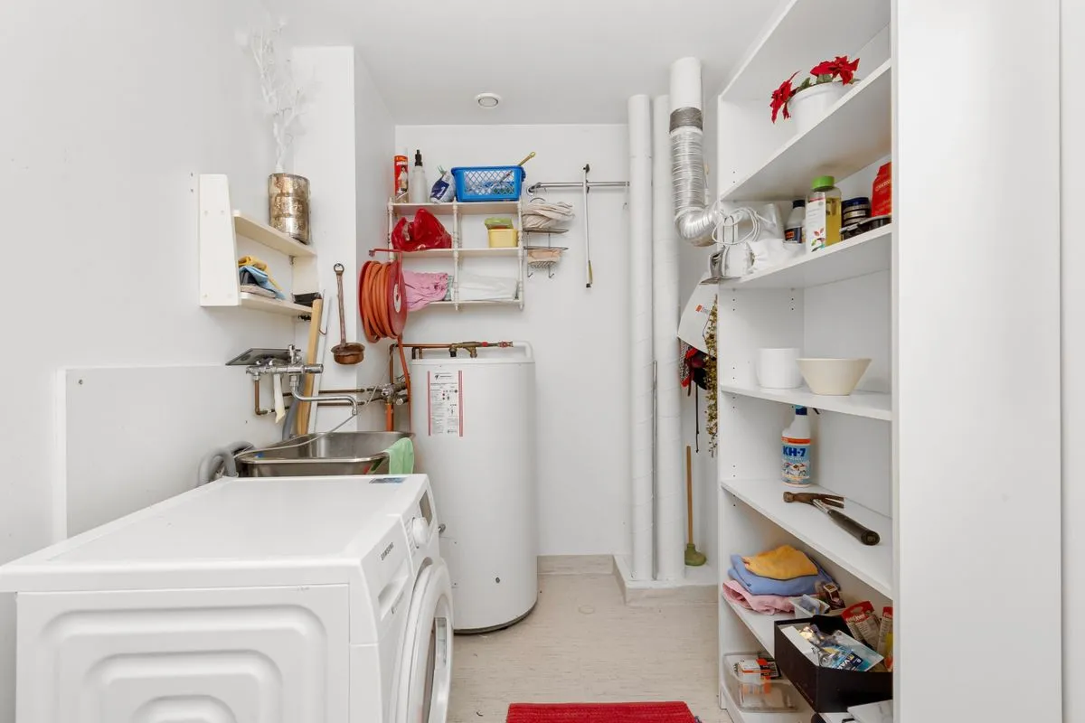 White cylindrical storage water heater tank standing beside a washing machine in a small utility storage room