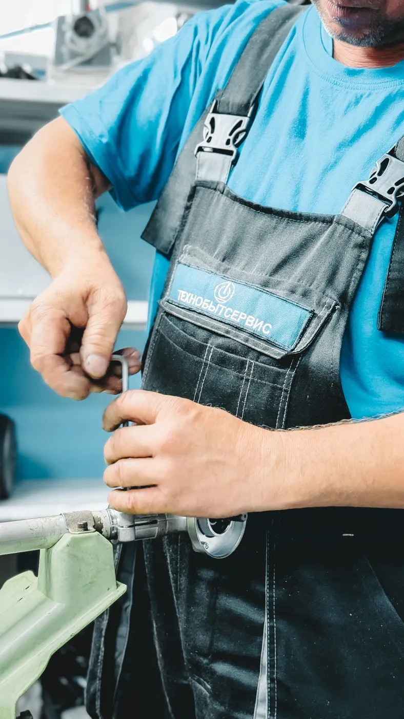 Plumber in blue overalls using a wrench on a metal pipe fitting during a plumbing disconnection