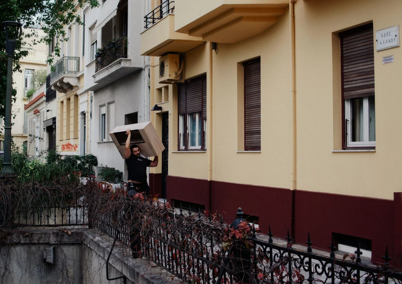 Man carrying a wooden cabinet on his shoulder along the pavement outside a residential apartment building