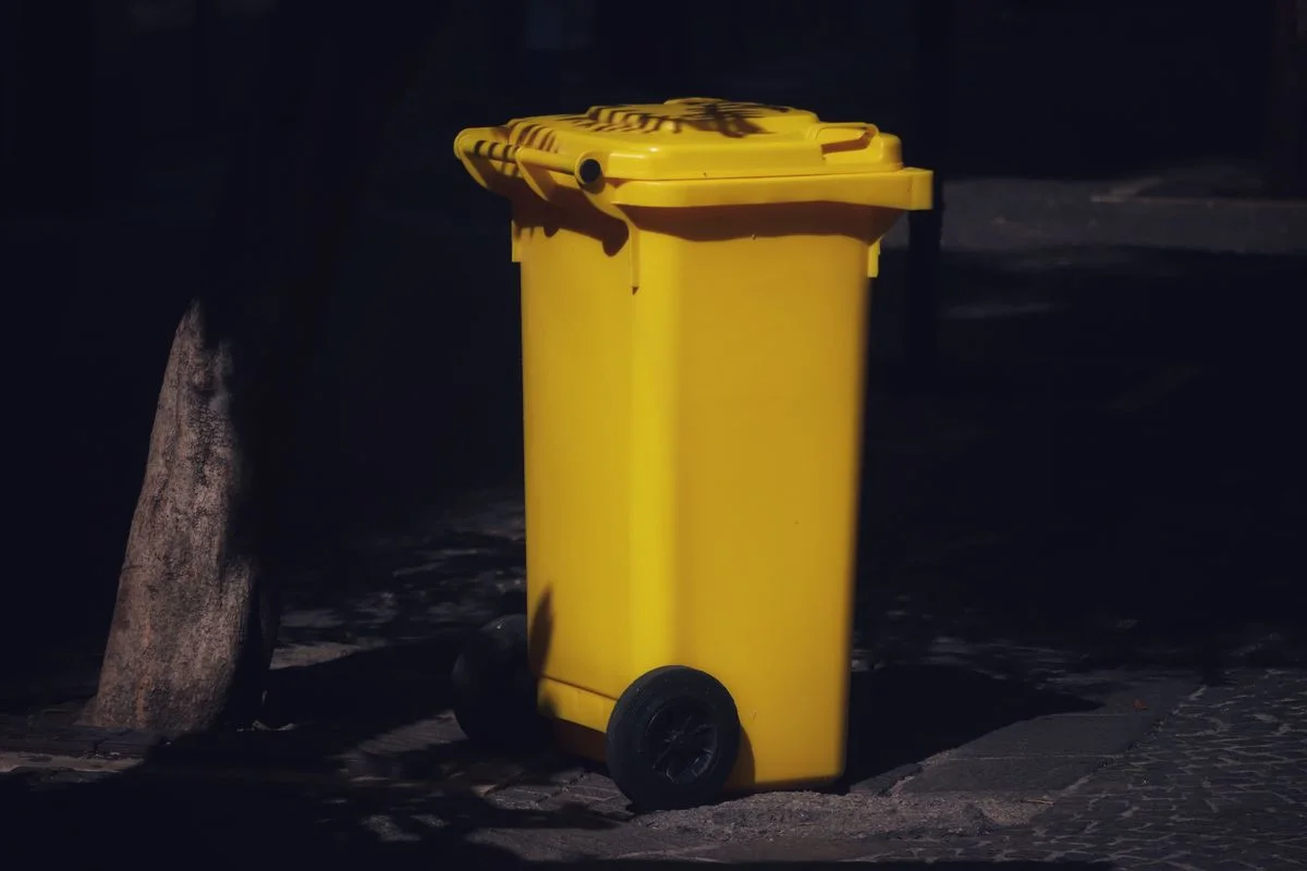 Sturdy outdoor wheeled refuse bin positioned in deep tree shade on stone pavers to keep waste out of direct sunlight